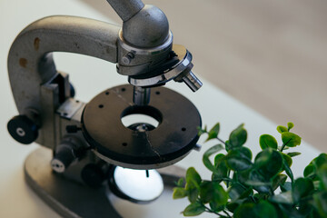 an old iron microscope is on the desktop in the office. equipment for studying microbes, viruses, biological samples of plants and humans. concept: studying epidemics and pandemics