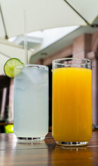 Vasos con agua de limón y jugo de naranja sobre mesa de madera / Glasses with lime water and orange juice on wooden table