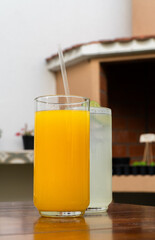 Vasos con agua de limón y jugo de naranja sobre mesa de madera / Glasses with lime water and orange juice on wooden table
