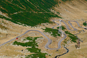 Close-up view of winding Transfagarasan road with red cable car and pylons in Romanian mountains. Mountain serpentine of Balea River and Transfagarasan Highway.