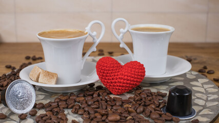 Romantic coffee scene with two white cups, coffee beans and knitted red heart on wooden table