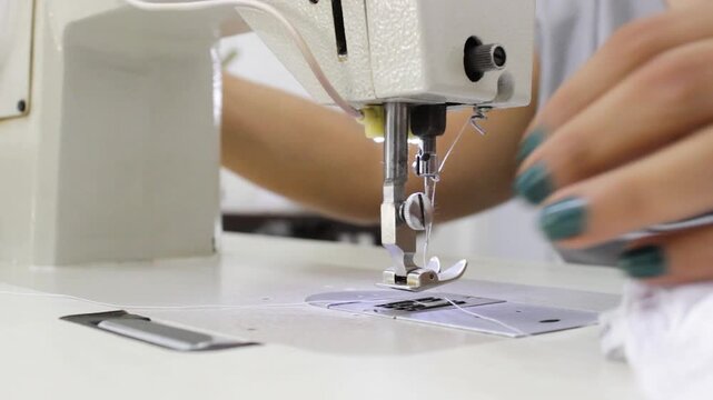 An unrecognizable woman's hands thread a white thread through a needle on a sewing machine inside a clothing production hall in Neiva, Huila, Colombia. Concept of handmade and industrial production