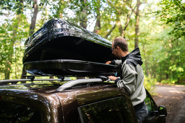 Man Attaching or Opening a Black Roof Box on a Car in the Forest