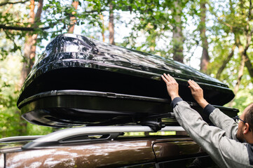 Man Attaching or Opening a Black Roof Box on a Car in the Forest