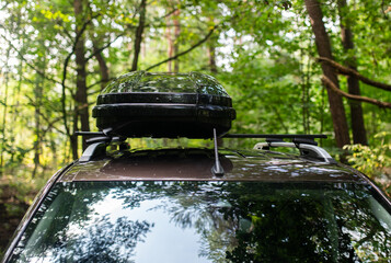 Man Attaching or Opening a Black Roof Box on a Car in the Forest