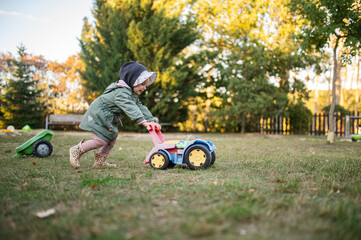 Toddler Girl Pushing a Toy Tractor Walker in the Backyard