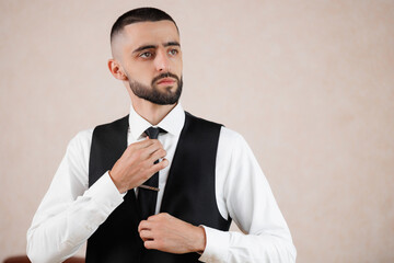 Man adjusts his tie while wearing a formal suit in a light-colored room