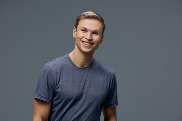 Smiling happy young man wearing casual blue t-shirt looking at camera isolated on gray background friendly mood communication concept