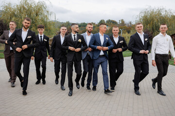 Group of groomsmen walking together in formal attire at a wedding celebration outdoors