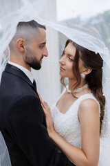 Couple sharing a tender moment under a veil during their wedding ceremony in a romantic setting