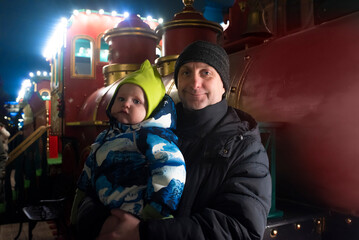 A father and his little son stand near a Christmas red train at night