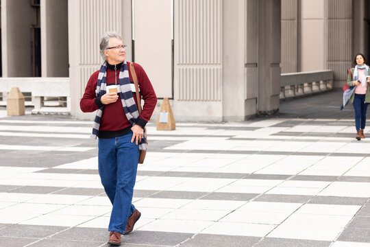 Diverse senior pedestrians walking plaza, carrying crossbody bag and holding coffee cup, copy space