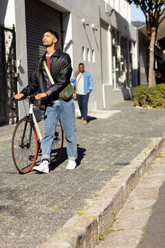 African American man pushing bicycle on street beside shutter while companion holding smartphone