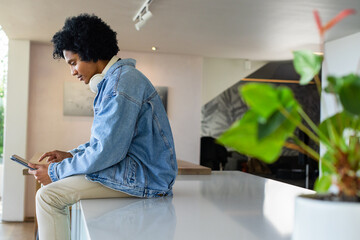 African American man sitting on counter in living area using digital tablet wearing headphones