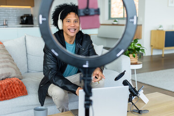 African American man sitting on sofa speaking into microphone by ring light in living room