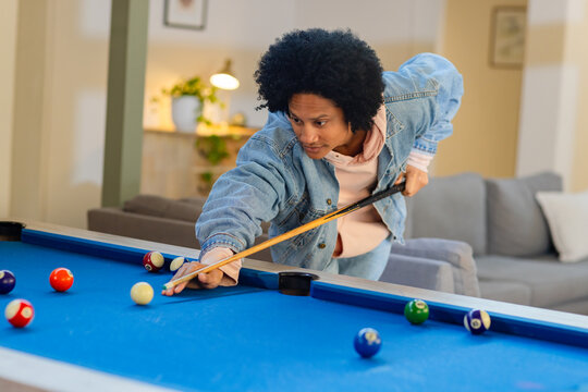 African American man leaning over pool table at home, lining up cue shot among billiard balls