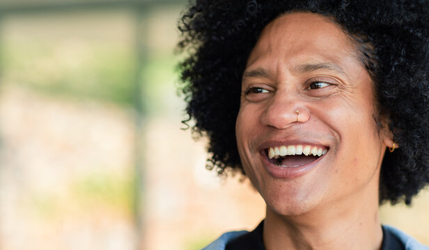 African American male wearing nose ring, hoop earring smiling in room near window frame, copy space