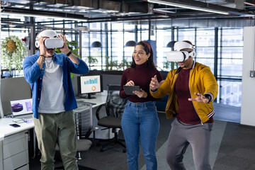 Diverse colleagues collaborating using VR headsets analyzing chart data on office monitors