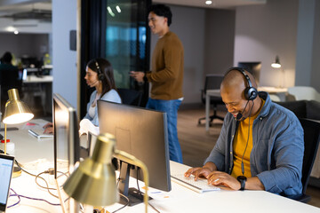 Diverse coworkers typing in open plan office with headsets and checking smartphone, copy space