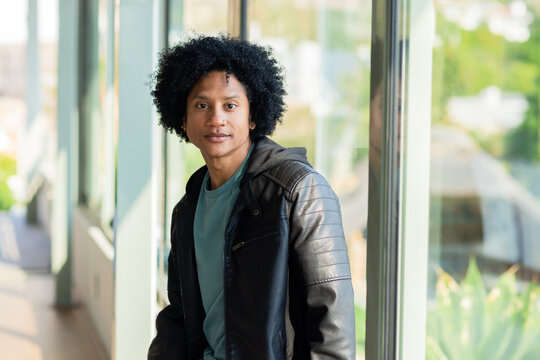 African American man leaning against floor-to-ceiling glass wall in corridor columns and reflection