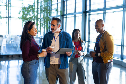 Diverse colleagues wearing badge lanyards while holding coffee cups and tablet in conference lobby