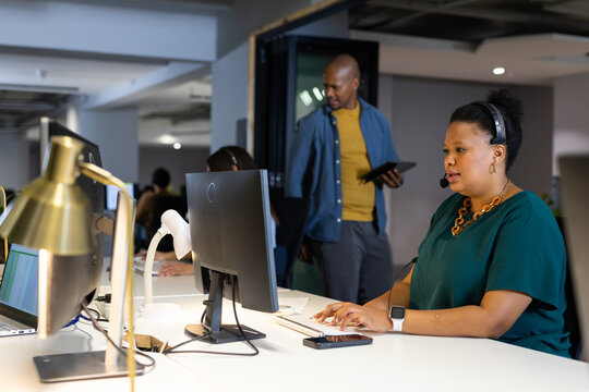 Diverse coworkers using monitors in modern office typing on keyboard and holding tablet, copy space