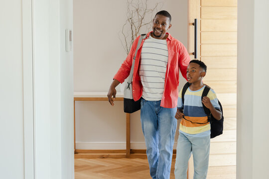 African American father and son entering home entryway carrying black shoulder bag and backpack