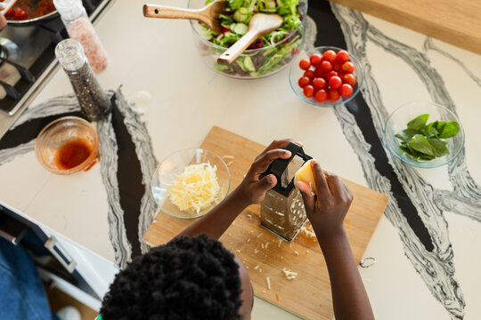 African American mother and son grating cheese with box grater, stirring salad in home kitchen