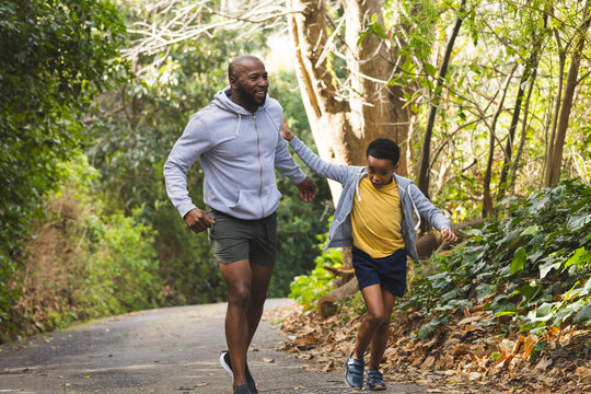 African American father and son running together on paved forest trail passing scattered leaves - Powered by Adobe