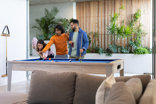 Friends leaning and crouching around pool table lining up shot with pool cues in lounge