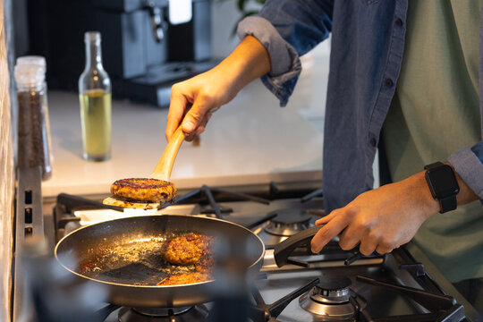 Wooden spatula lifting browned patty from nonstick pan on gas stove with oil bottle, coffee machine