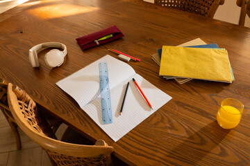 Open lined notebook sitting centered on wooden dining table with blue ruler and pencils