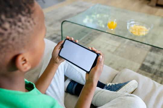 Smartphone is resting horizontally on sofa in living room, with chips and juice on table