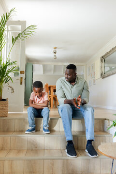 African American father and child sitting on tiled steps inside home, father gesturing near plant