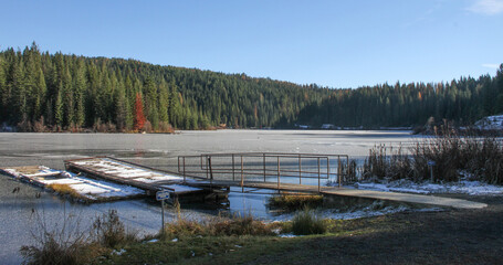 photo of ice on Elk River Reservoir in Idaho mountains with a background of trees and forest and foreground with a fishing dock