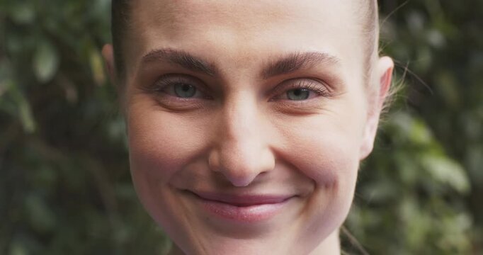 Woman reacting to opening shot by smiling into wide grin in front of dense foliage outdoors