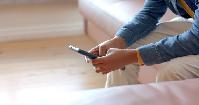 Lowering onto sofa in living room, smartphone user composing message with repeated taps and swipes