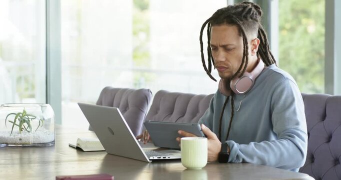 Man noticing laptop alert grabbing tablet scrolling content to compare data at dining table
