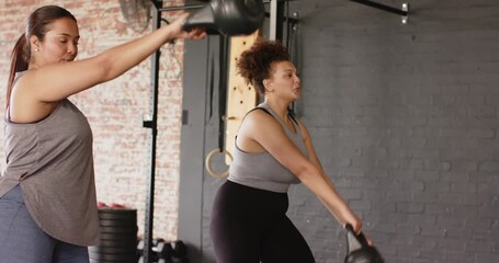 After partner starting swing Diverse female duo performing black kettlebell training in gym - Powered by Adobe