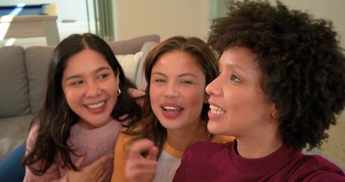 Diverse female friends on sofa seeing smartphone pouting laughing posing peace signs puckering lips