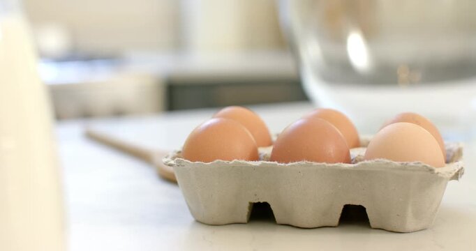 Camera is shifting focus to eggs and spoon near mixing bowl on countertop for baking prep