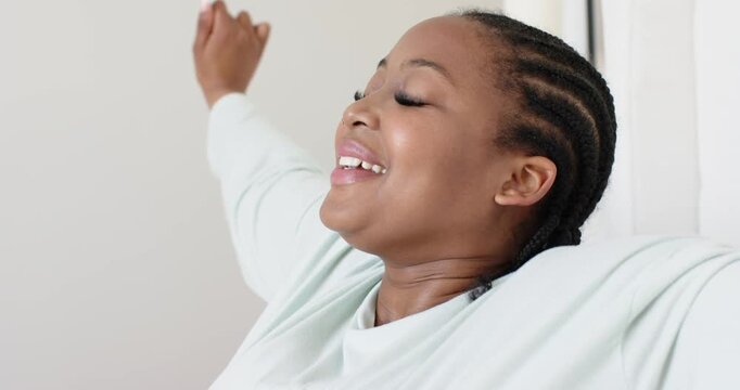 After sitting, African American woman raising arms and arching back, relieving tension in bedroom