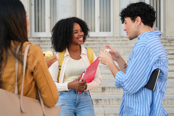 Diverse students laughing, eating snacks, and chatting on university campus stairs