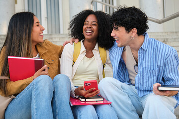 Group of diverse college students sitting on campus stairs, laughing and having fun together