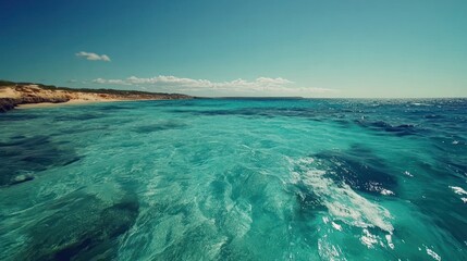 Crystal clear turquoise water meets a sandy beach under a bright blue sky with scattered clouds