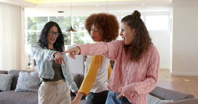 Diverse female friends following right woman pointing up while dancing on sofa for fun