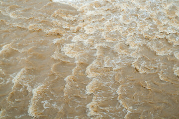 Close-Up Of Turbulent Muddy Water With White Foam And Swirling Texture