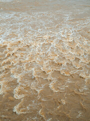 Close-Up Of Turbulent Muddy Water With White Foam And Swirling Texture