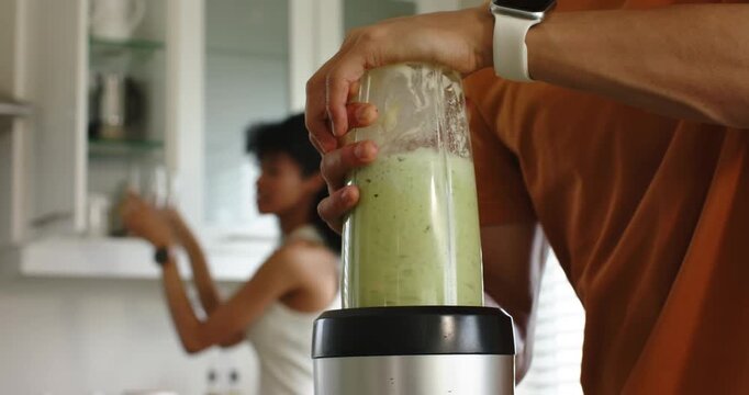 Diverse couple man placing blender on base holding blending smoothie to serve woman holding glasses