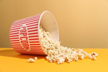 Tasty popcorn in paper cup on orange table against beige background, closeup